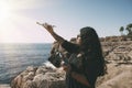 happy woman with drone, looking to the side black dress and remote control, on cliff, by the sea sunny day. technological concept