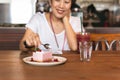 Happy woman eating currant mousse cake with spoon in cafe.