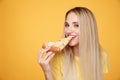 Happy woman eating tasty pizza for lunch in the yellow studio.