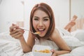 Happy woman enjoying cornflakes cereals in the bedroom