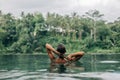 Woman enjoying tropical rain while swimming in infinity pool on Bali