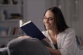 Happy woman with eyeglasses reading book in the night