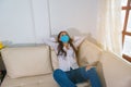 Happy woman with face mask resting comfortably sitting on a couch in the living room at home Royalty Free Stock Photo