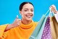 Happy woman, face and shopping bags with thumbs up for purchase, sale or discount against a blue studio background Royalty Free Stock Photo