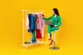 Happy woman fashion designer with laptop looking at clothes on warbrobe rack, using laptop computer, yellow background
