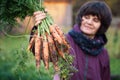 Happy woman gardener holds in her hand a bunch of fresh dirty carrots outdoors Royalty Free Stock Photo