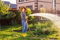 Happy woman gardener in work clothes watering the beds in her vegetable garden on sunny warm summer day. Concept of