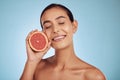 Happy woman, grapefruit and vitamin C for skincare or diet against a blue studio background. Face of female person with