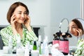 Happy woman in green long-sleeve poses at mirror touching face