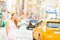 A happy woman hailing a yellow taxi while walking on a street in New York city Royalty Free Stock Photo