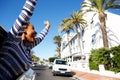 Happy woman hanging outside car window with arms raised