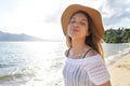 Happy woman with hat breathing and smiling at the beach on summer vacation. Beautiful young female with closed eyes enjoy nature Royalty Free Stock Photo