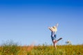 Happy woman in hat jumping in green field against blue sky