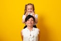 Happy woman, have fun with cute child baby girl. Mommy little kid daughter stand behind hug, isolated on yellow background.