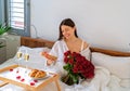 Happy woman having surprise gift and romantic breakfast in bed on Valentine Day holding present Royalty Free Stock Photo