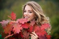 Happy woman holding autumn leafs on face in fall nature. Portrait of young woman with autumn maple leaves outdoor Royalty Free Stock Photo