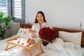 Happy woman holding bouquet of flowers excited about surprise gift and romantic breakfast in bed on Valentine Day Royalty Free Stock Photo