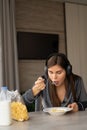 Happy woman holding bowl and spoon eating cereal while sitting at home. listen to music in wireless headphones during Royalty Free Stock Photo