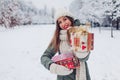 Happy woman holding Christmas presents gift boxes in snowy winter park offering one. Festive holiday season. Space Royalty Free Stock Photo