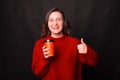 A happy woman is holding a cup of hot drink and laughing at camera is showing a thumb up Royalty Free Stock Photo