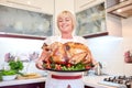 Happy woman holding garnished roasted turkey on a kitchen background. Thanksgiving turkey concept. Copy space.