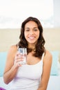 Happy woman holding glass of water while sitting on bed Royalty Free Stock Photo