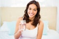 Happy woman holding glass of water while sitting on bed Royalty Free Stock Photo