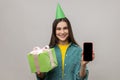 Happy woman holding wrapped present box and smart phone with blank screen for advertisement. Royalty Free Stock Photo