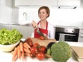 Happy woman at home kitchen preparing vegetable salad with lettuce, carrots and slicing tomato smiling Royalty Free Stock Photo