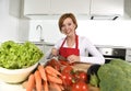 Happy woman at home kitchen preparing vegetable salad with lettuce carrots and slicing tomato Royalty Free Stock Photo