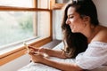 Happy woman at home texting in her mobile phone in bright bedroom. Checking social apps with smartphone. Lifestyle concept