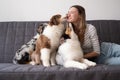 Happy woman kissing with three merle colours Australian shepherd puppy dog on couch Royalty Free Stock Photo