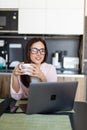 Happy woman in the kitchen reading he news on her laptop drinking morning coffee Royalty Free Stock Photo