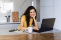 Happy young woman in the kitchen reading he news on her laptop Royalty Free Stock Photo