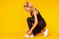 Happy Woman Lacing Shoes Before Workout On Yellow Background