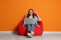 Happy woman with laptop sitting on beanbag chair near orange wall Royalty Free Stock Photo