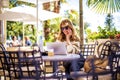 Happy woman with laptop sitting at outdoor cafe in city center and making a call Royalty Free Stock Photo