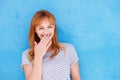 Happy woman laughing with hand to mouth against blue wall