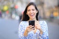 Happy woman laughing holding phone looking at you in the street Royalty Free Stock Photo