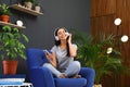 Happy woman listening to music in armchair. Indoor plants for trendy interior design