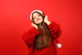 Happy woman listening to music with headphones wearing santa hat on red background. Enjoy holiday songs Royalty Free Stock Photo