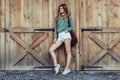 Happy woman with long legs look to the side near barn on the farm wearing casual outfit with shorts, backpack and sneakers. Royalty Free Stock Photo