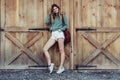 Happy woman with long legs look to the side near barn on the farm wearing casual outfit with shorts, backpack and sneakers.