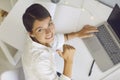 Happy woman looking at camera, smiling and showing thumbs-up while working on laptop