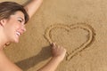 Happy woman in love drawing a heart on the sand of the beach