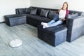 People, housework and technology concept. Happy woman lying on the couch while robot vacuum cleaner clean home Royalty Free Stock Photo