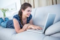 Happy woman lying on couch using her laptop Royalty Free Stock Photo
