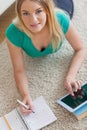 Happy woman lying on floor doing her homework using tablet Royalty Free Stock Photo