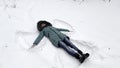 Happy woman lying on snowy lawn at forest and making angel. Young girl playing in snow and enjoying wintertime. Cheerful