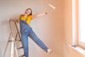 Happy woman makes repairs in her apartment. Funny female with a roller on ladder with copy space. Independent single